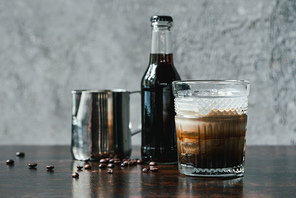 cold brew coffee with milk in glass near bottle, milk jug and coffee beans on wooden table