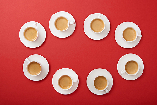 top view of white cups with tasty coffee on saucers on red background