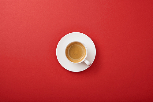 top view of white cup with coffee on saucer on red background