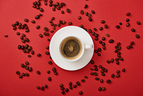 top view of delicious coffee in cup near scattered roasted beans on red background