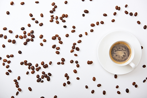 top view of delicious coffee in cup near scattered roasted beans on white background