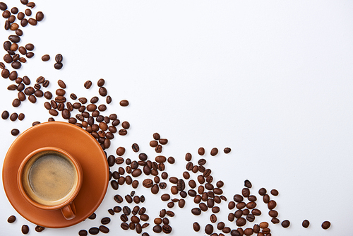 top view of delicious coffee in cup near scattered beans on white background with copy space