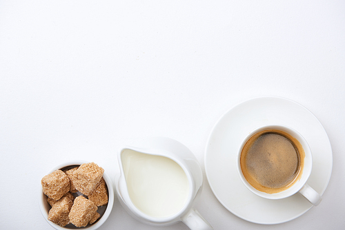 top view of tasty coffee in cup on saucer near milk and brown sugar on white background