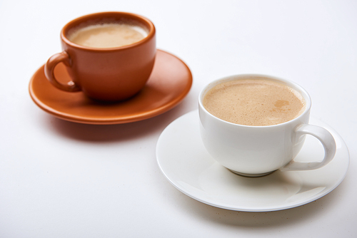 selective focus of delicious coffee with foam in cups on saucers on white background
