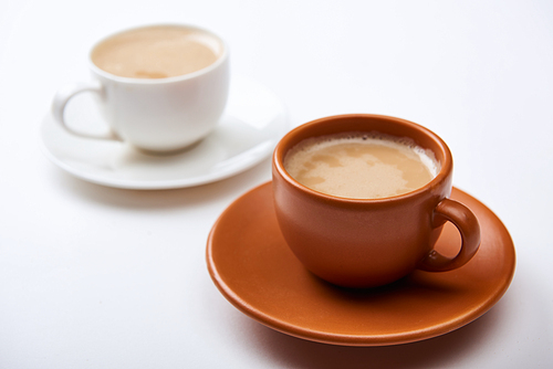 selective focus of coffee with foam in cups on saucers on white background