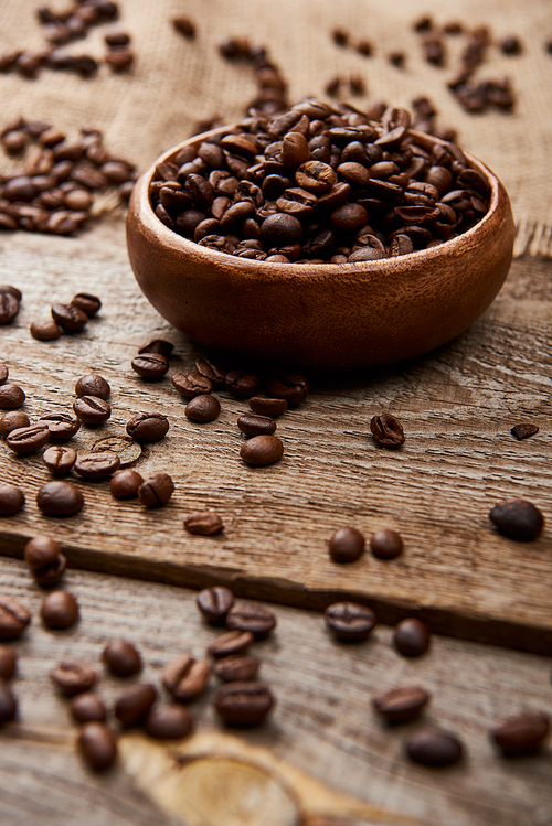 selective focus of fresh roasted coffee beans scattered near bowl on wooden board