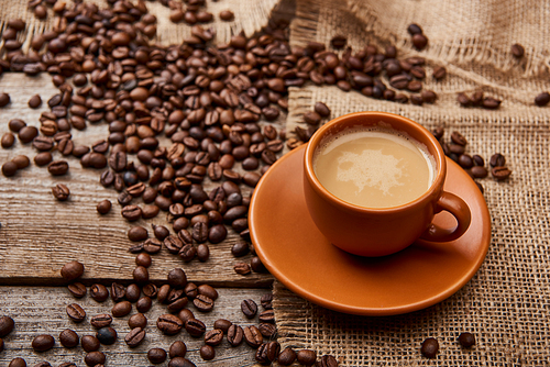coffee beans near cup of coffee on wooden background