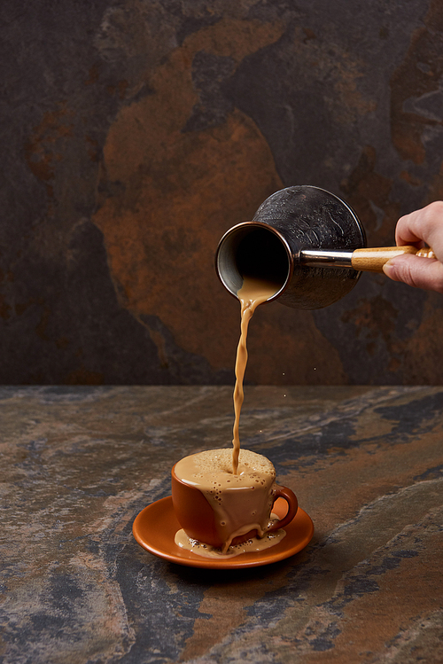 partial view of man pouring coffee from cezve in cup on marble surface