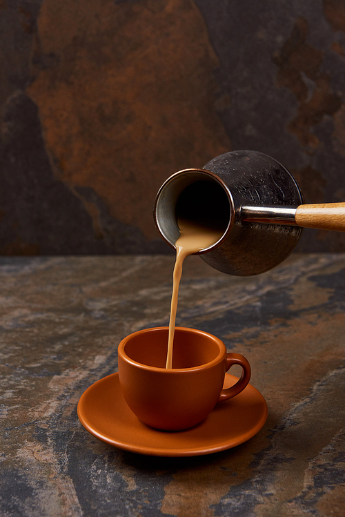 pouring coffee from cezve into cup on marble surface