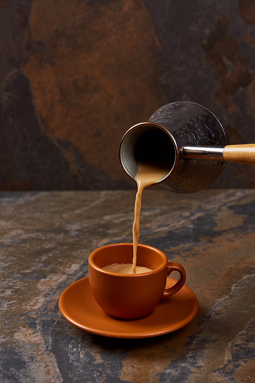 pouring hot coffee from cezve into cup on marble surface