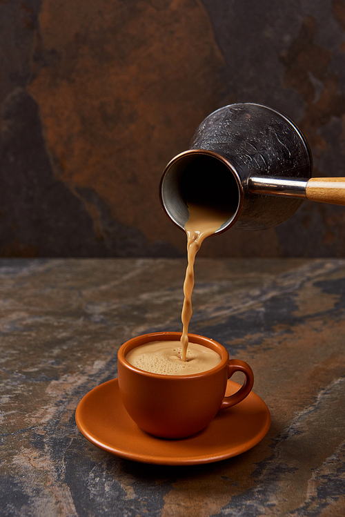 pouring coffee from cezve into brown cup on marble surface