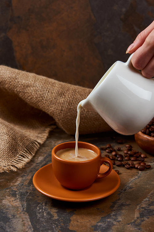 cropped view of woman pouring milk in cup with coffee on marble table