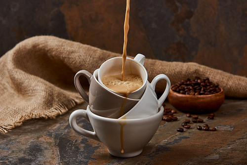 flowing out hot coffee from cups on marble surface near sackcloth and beans