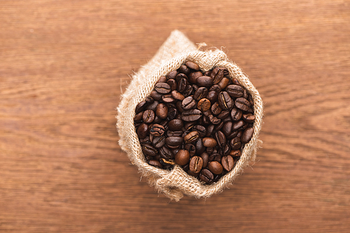 selective focus of fresh roasted coffee beans in sack on wooden surface