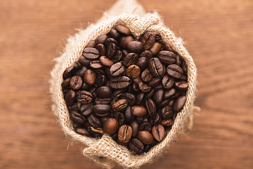 selective focus of fresh roasted coffee beans in sack on wooden surface