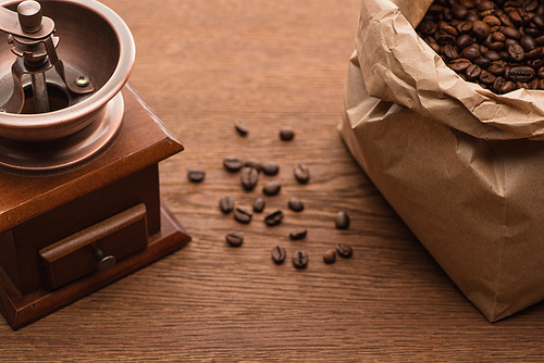 selective focus of fresh roasted coffee beans in paper bag near coffee grinder on wooden table