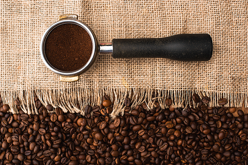 top view of fresh roasted coffee beans and sackcloth with filter holder with ground coffee