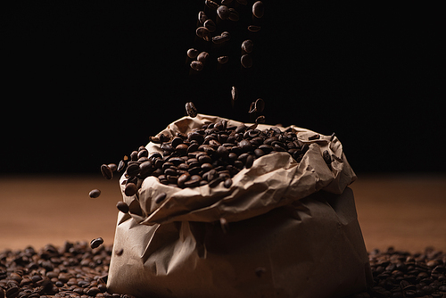 roasted coffee beans falling in bag on black background