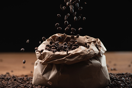 roasted coffee beans falling in bag on black background