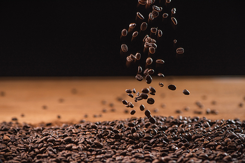 roasted coffee beans falling on pile on black background