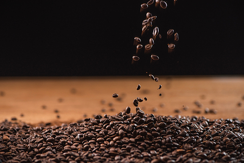 fresh roasted coffee beans falling on pile on black background