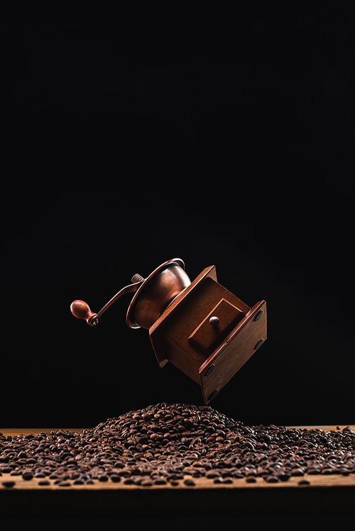 coffee grinder above fresh roasted coffee beans isolated on black