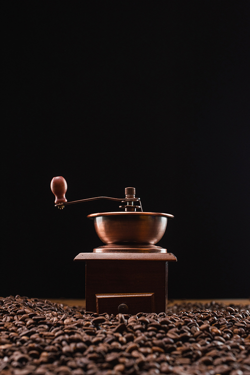 selective focus of coffee grinder on fresh roasted coffee beans isolated on black