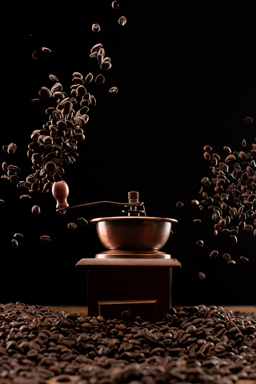coffee grinder and fresh roasted coffee beans in air isolated on black
