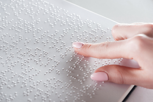 partial view of young woman reading braille text on white paper
