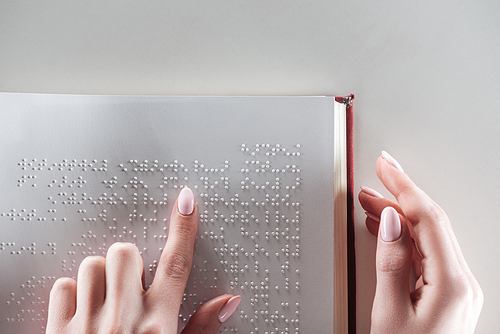 top view of young woman reading braille text on white paper