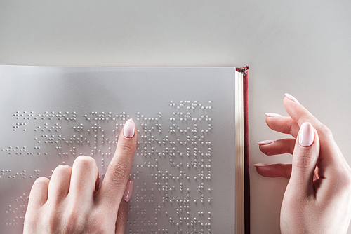 top view of young woman reading braille text on white paper