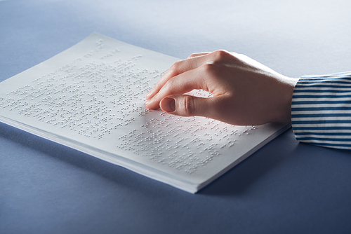 cropped view of young woman reading braille text with hand on blue