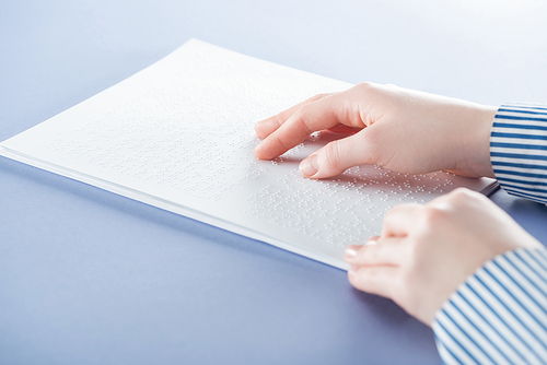 cropped view of young woman reading braille text with hand isolated on violet