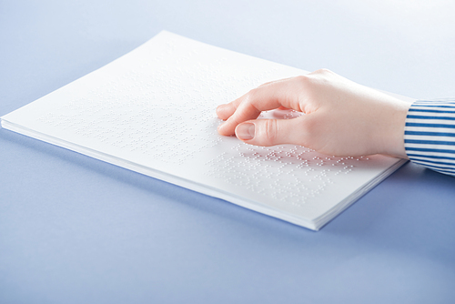 cropped view of young woman reading braille text with hand isolated on violet