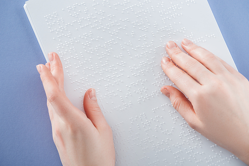 partial view of young woman reading braille text with hand isolated on violet