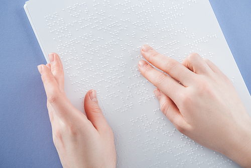 partial view of young woman reading braille text with hand isolated on violet