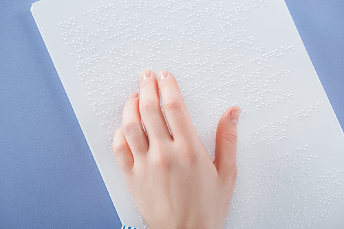 top view of young woman reading braille text with hand isolated on violet