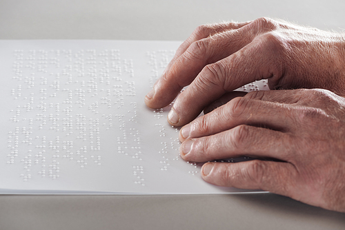 partial view of senior man reading braille text isolated on grey