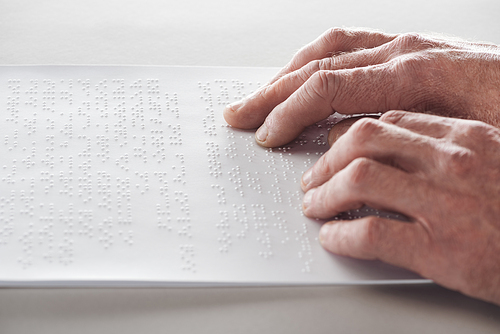 cropped view of senior man reading braille text isolated on grey