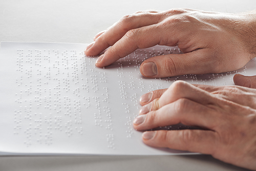 cropped view of man reading braille text with hands isolated on grey
