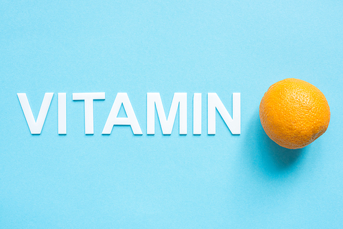 top view of ripe orange and word vitamin on blue background