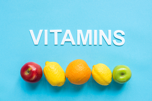 top view of ripe fruits in line and word vitamins on blue background