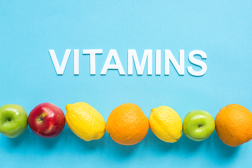 top view of ripe fruits in line and word vitamins on blue background