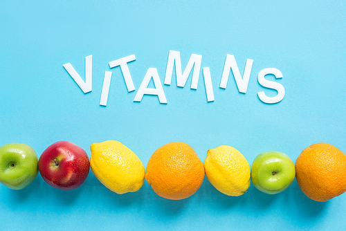 top view of ripe fruits and word vitamins on blue background