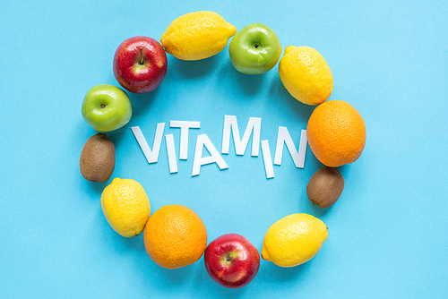 top view of ripe fruits around word vitamin on blue background