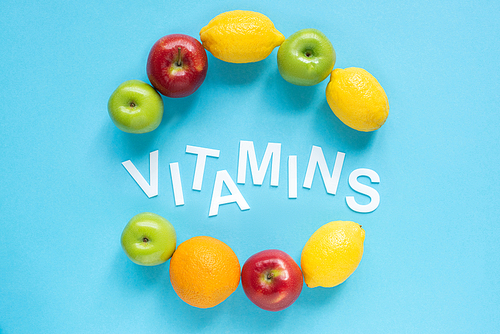 top view of ripe fruits around word vitamins on blue background