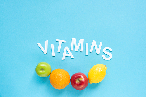 top view of ripe fruits and word vitamins on blue background