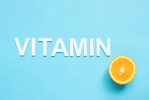 top view of ripe orange half and word vitamin on blue background
