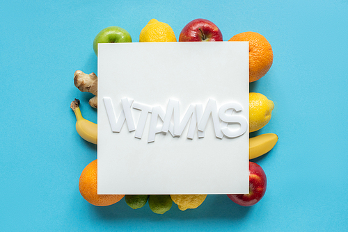top view of ripe fruits and word vitamins on white paper on blue background
