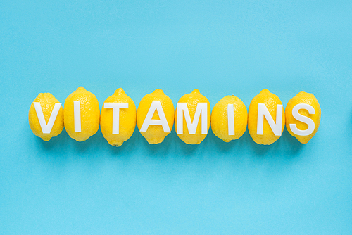 top view of ripe yellow lemons and word vitamins on blue background